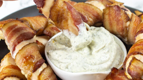 hand dipping a bacon wrapped chicken tender into a small dish of ranch dip
