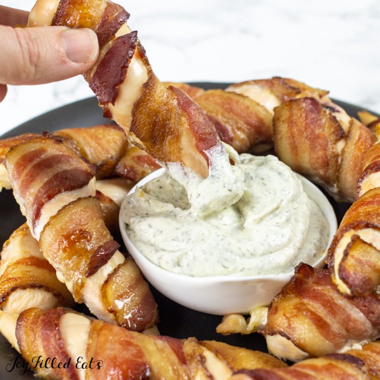 hand dipping a bacon wrapped chicken tender into a small dish of ranch dip