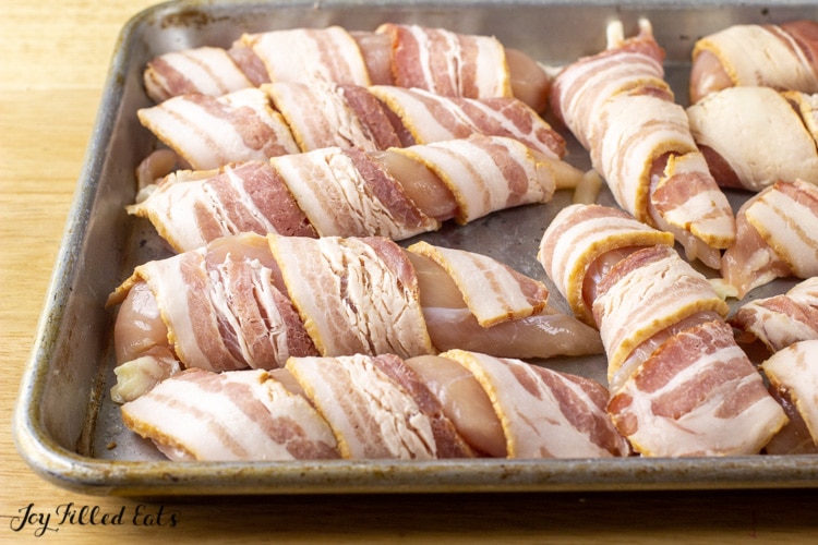 bacon wrapped around chicken tenderloins on small baking sheet