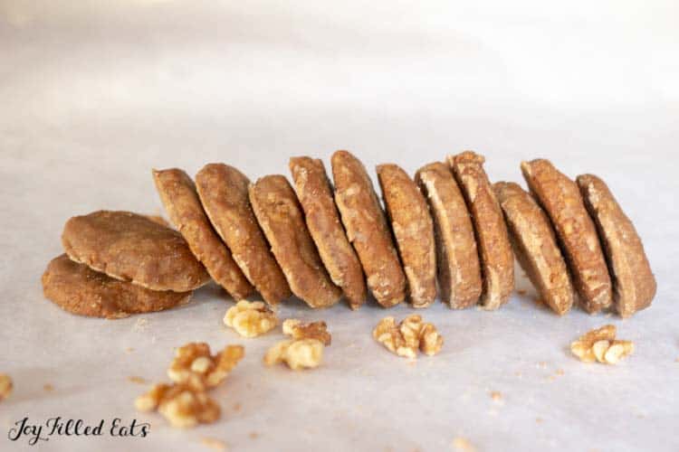 Glazed Maple Walnut Cookies arranged upright in a row, leaning on each other surrounded by scattered raw walnut pieces