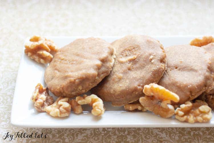 white, rectangular plate of glazed maple walnut cookies fanned out surrounded by whole, raw walnuts