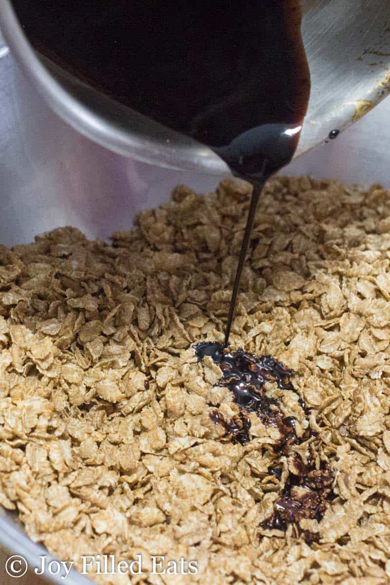 chocolate and sweetener mixture being poured onto plain cereal on a sheet pan