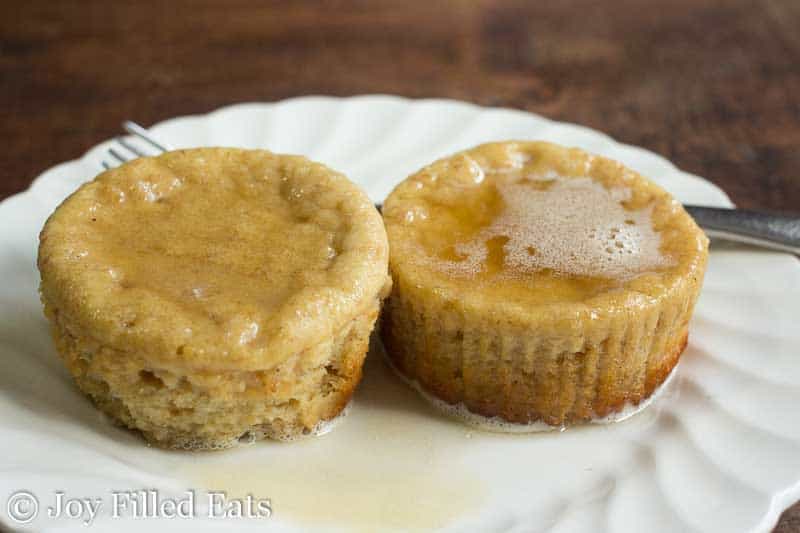 two warm chai pancake muffins on a white plate and topped with a glaze of chai butter