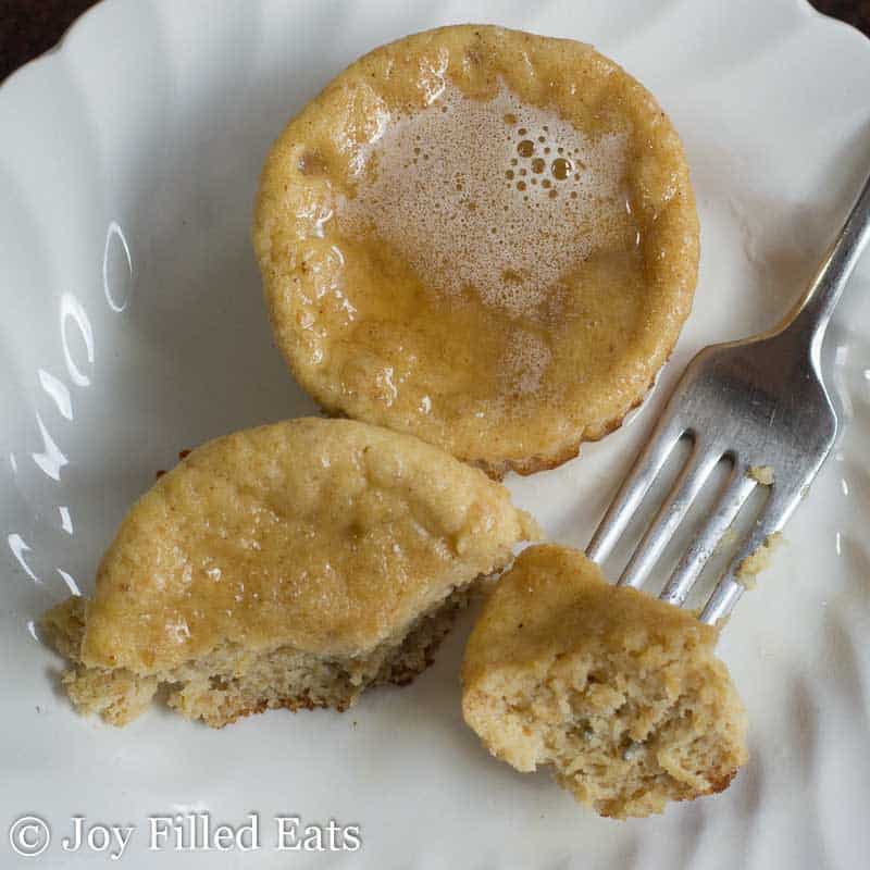 overhead view of two warm chai pancake muffins on a white plate with one muffin cut in half and bite of muffin on fork
