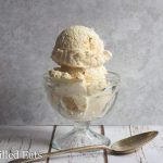 two scoops of slated caramel ice cream in a glass ice cream bowl set next to a spoon
