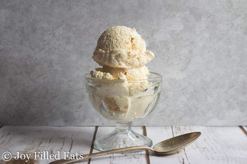 two scoops of slated caramel ice cream in a glass ice cream bowl set next to a spoon