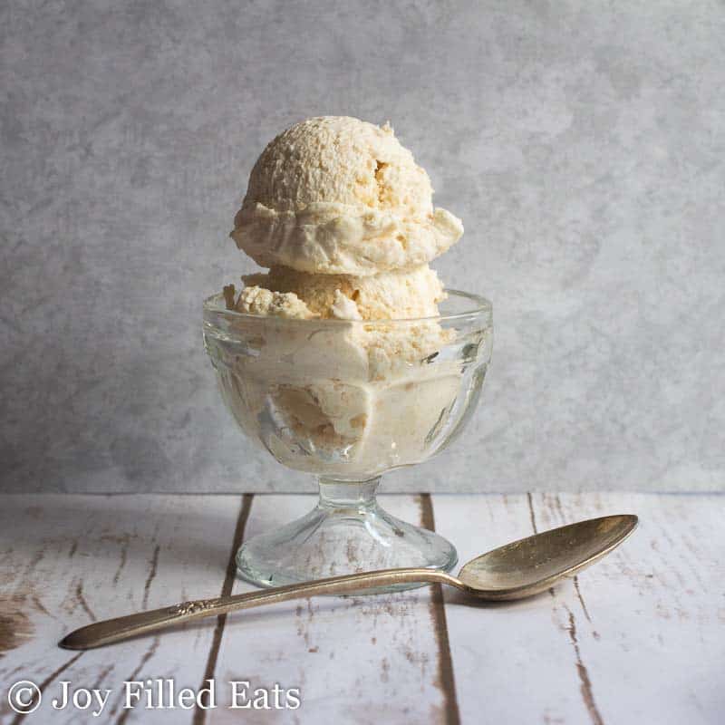 two scoops of salted caramel ice cream in a glass bowl set next to a spoon