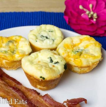 four mini quiches and two strips of bacon on a white plate next to a flower