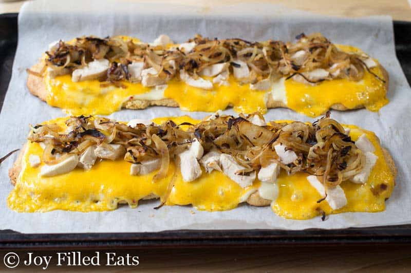 chicken and onion topped onto melted cheese and flatbread placed on parchment paper lined sheet pan