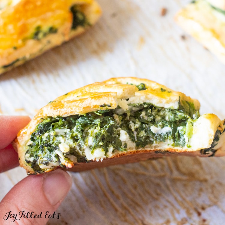 hand holding a spinach & feta pastries with a large bite missing