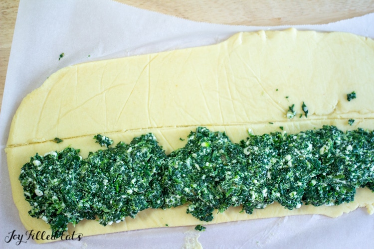 pastry dough rolled out onto parchment paper and half covered with a spinach and feta filling