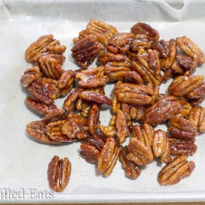 pile of glazed pecans on a parchment lined sheet pan