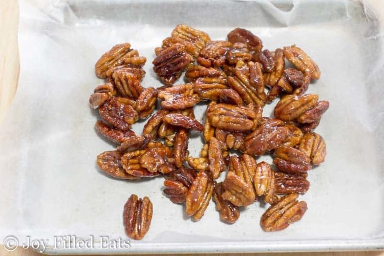 pile of glazed pecans on a parchment lined sheet pan
