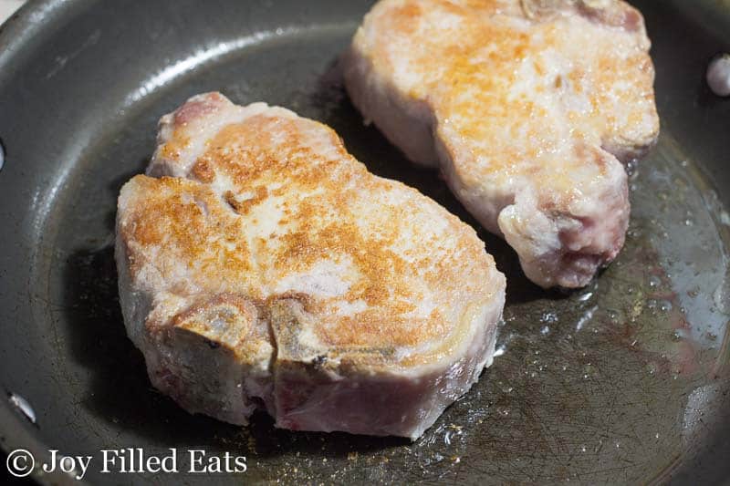 two pork chops browning in a skillet