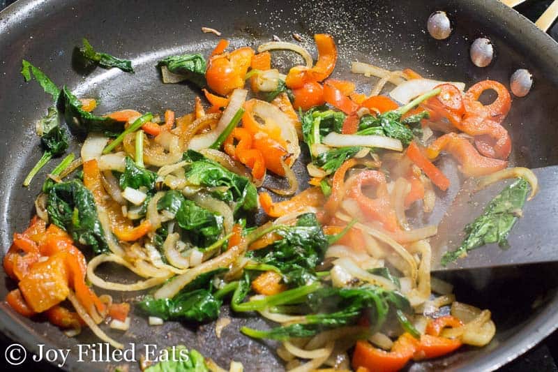 thinly sliced peppers, onions and spinach in a skillet