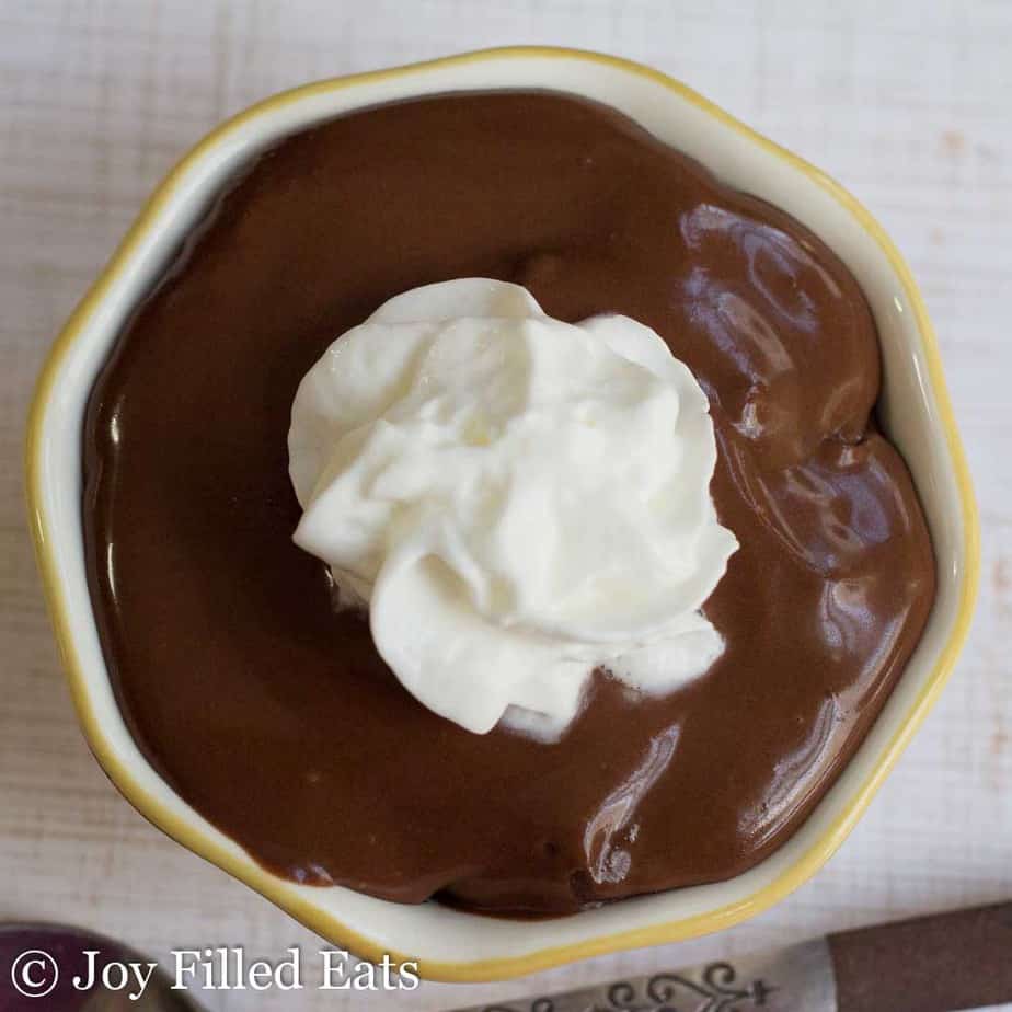 overhead view of rich chocolate pudding in a bowl and topped with whipped cream