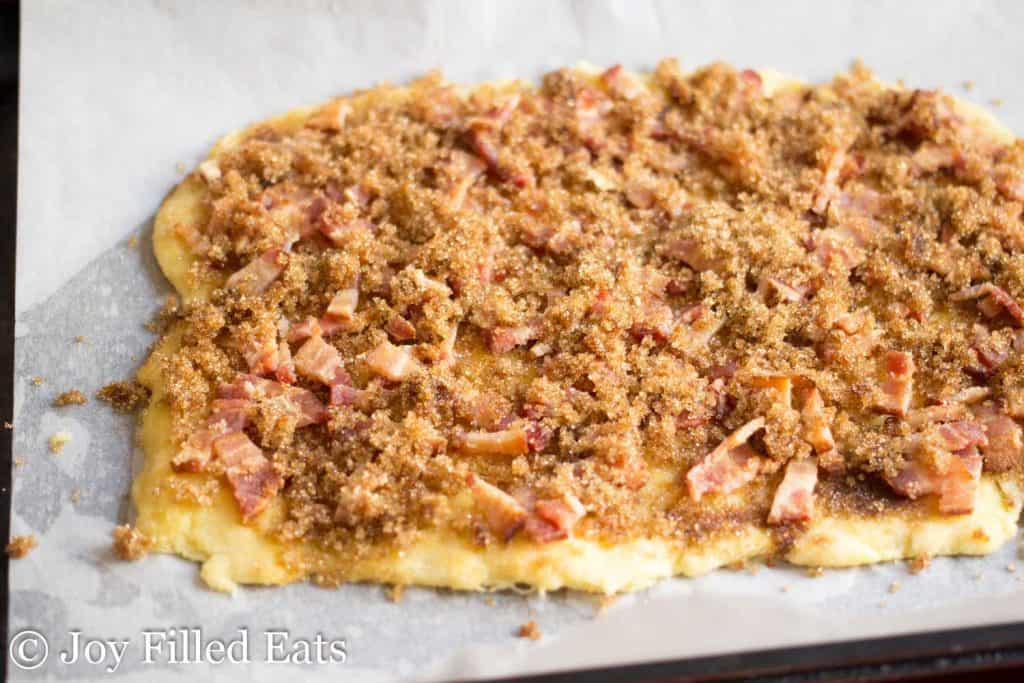 maple bacon crack dough rolled out onto parchment paper covered in toppings