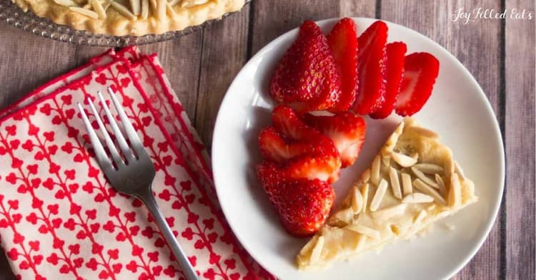 slice of almond tart on a plate with sliced strawberries set next to a fork and napkin