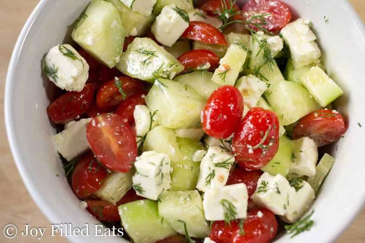 simple Greek tomato & cucumber salad in a white bowl close up