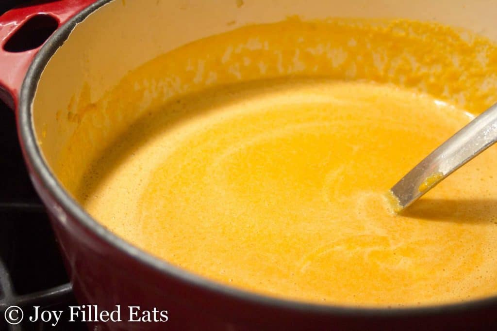 close up on pot of roasted red pepper soup with ladle