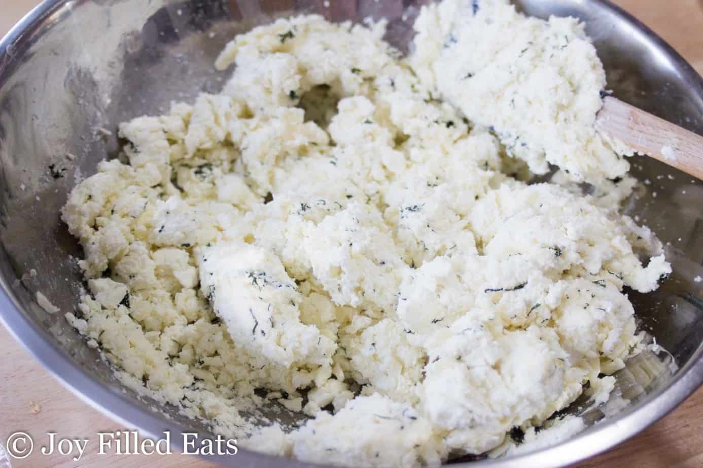 ingredients for feta & dill cheese ball being mixed in a large mixing bowl with spatula