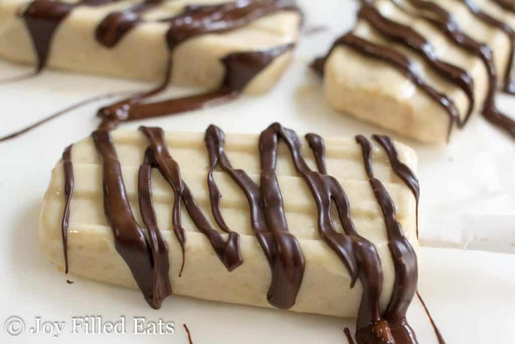 Peanut butter ice cream bars drizzled in chocolate laying on a table