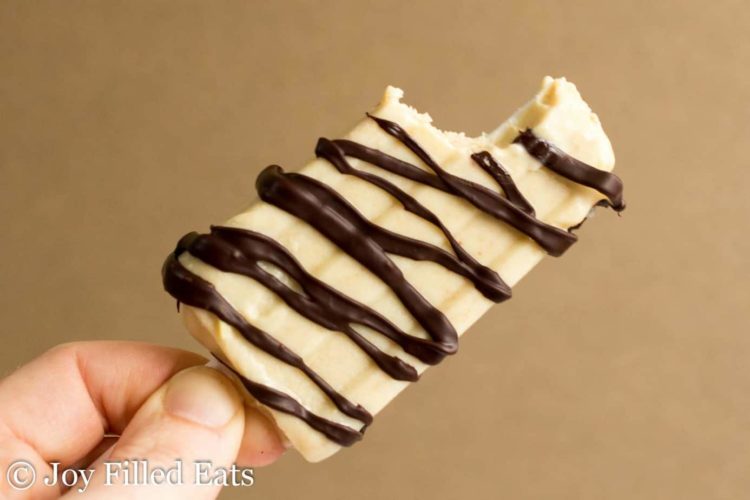 hand holding chocolate peanut butter ice cream bar with large bite missing