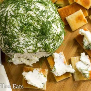 large Feta & dill Cheese ball on a cutting board with crackers and crackers spread with cheese