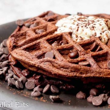 chocolate chocolate chip waffle surrounded by chocolate chips on a black plate