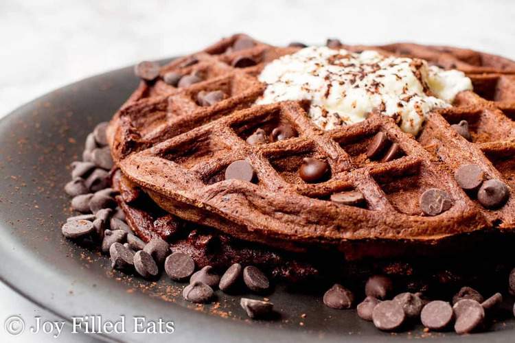 chocolate chocolate chip waffle surrounded by chocolate chips on a black plate
