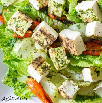 close up of grilled paneer on top of a green salad