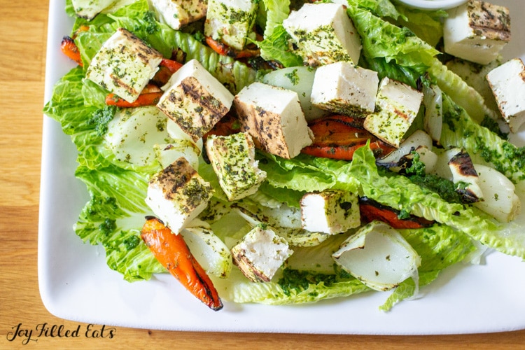 close up of grilled paneer on top of a green salad