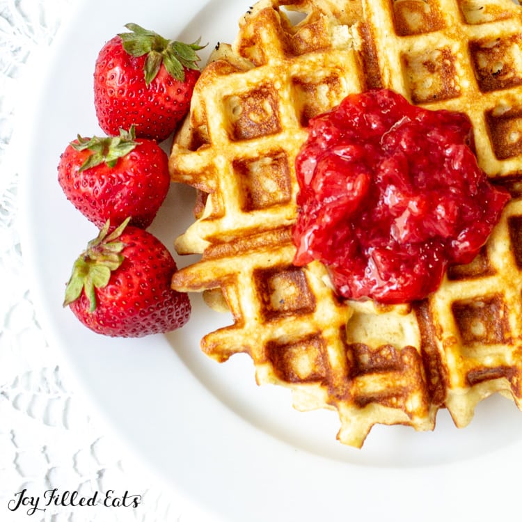 close up on keto strawberry jam centered on a waffle served with whole strawberries