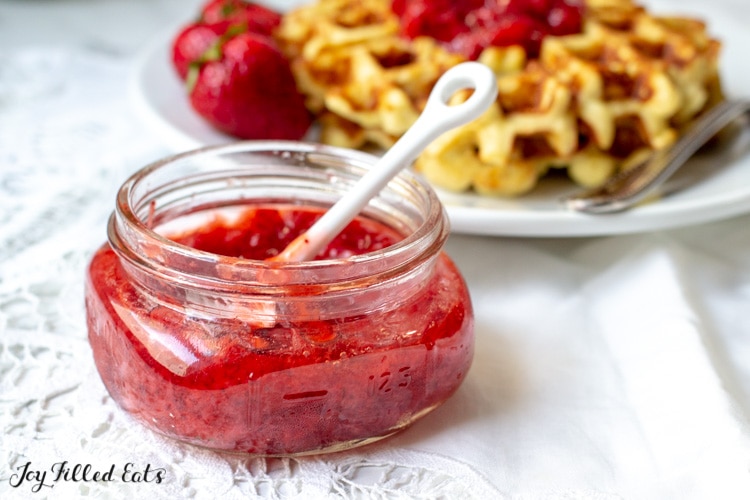 Glass jar of Fresh Strawberry Jam with waffles behind it