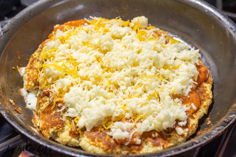 low carb pizza cooking in skillet and topped with grated cheese