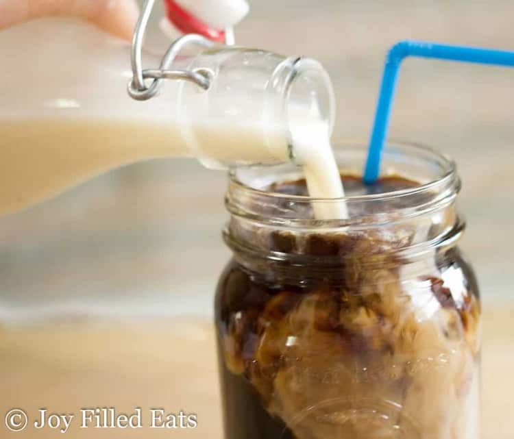 monfruit coffee cream being poured into a mason jar of iced coffee with blue straw