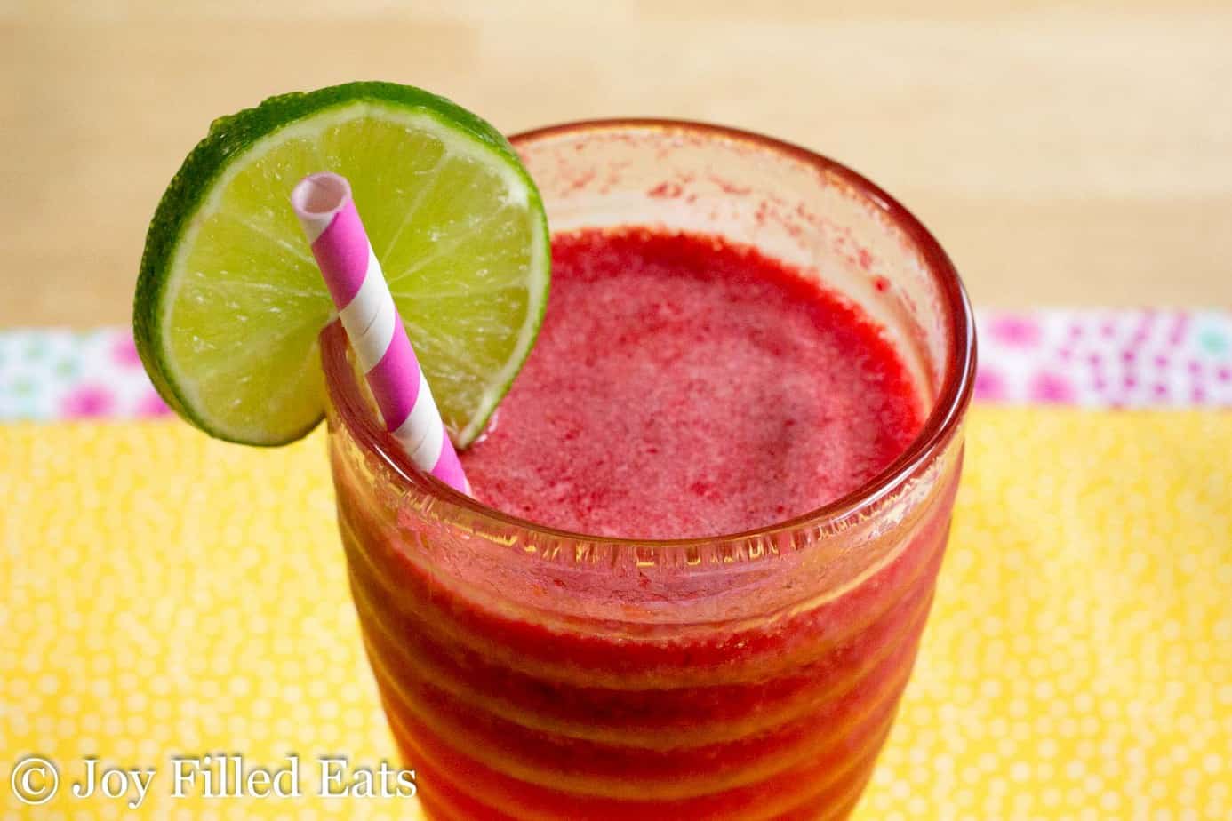 close up of sparkling raspberry lime soda with a lime slice on the rim with paper straw