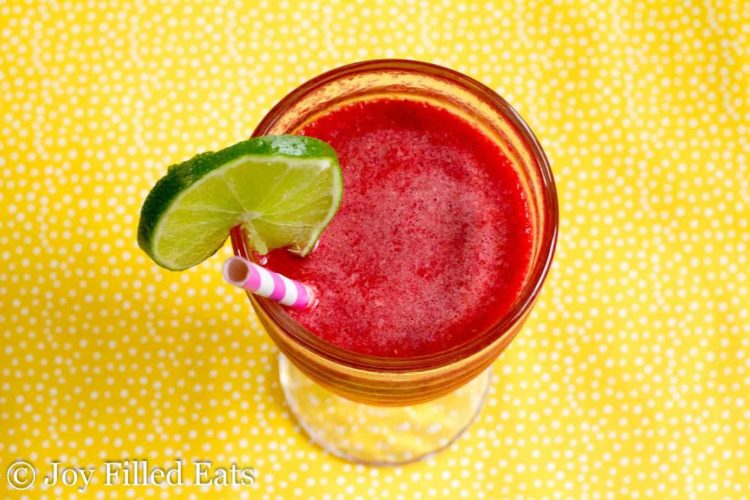 overhead view of sparkling raspberry lime soda with a lime slice on the rim with paper straw