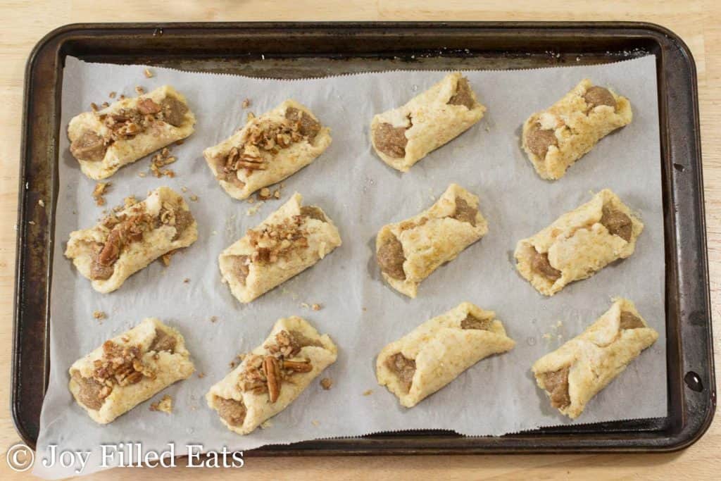 pecan danishes lined on a sheet pan before baking, half the danishes topped with chopped pecans