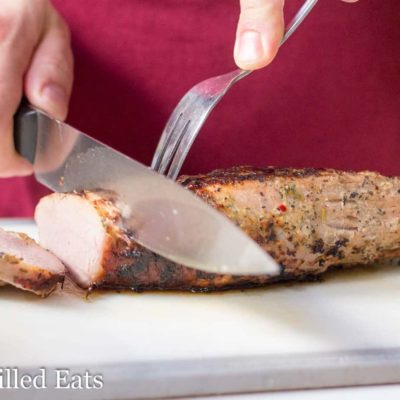 hand using carving knife and fork to slice pork tenderloin on cutting board