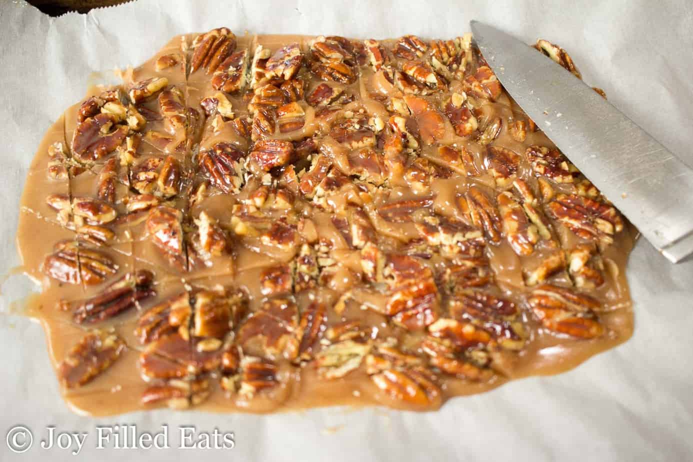 creamy pecan pralines spread onto parchment paper and roughly chopped with chef's knife