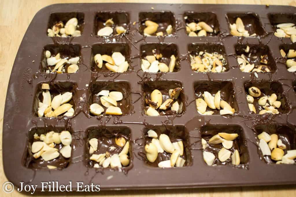 peanuts added into square moldings on tray lined with melted chocolate