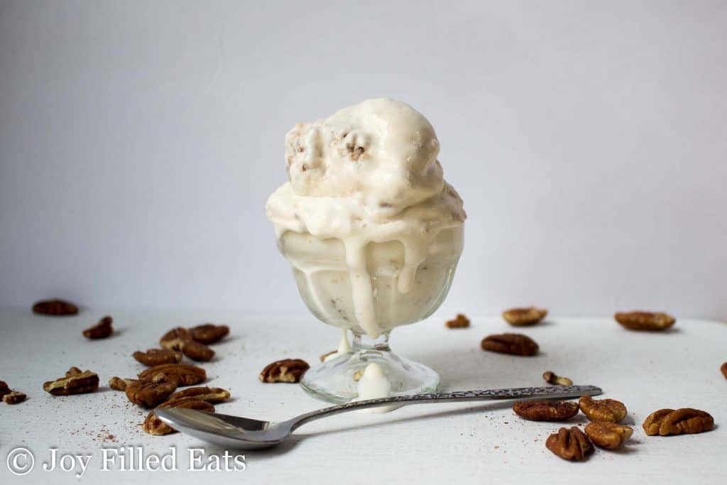 scoop of pecan praline ice cram in a glass ice cream cup melting down side and set behind a spoon