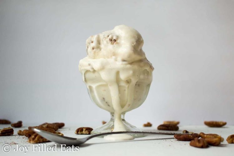 scoop of pecan praline ice cream melting down glass ice cream cup placed behind a spoon
