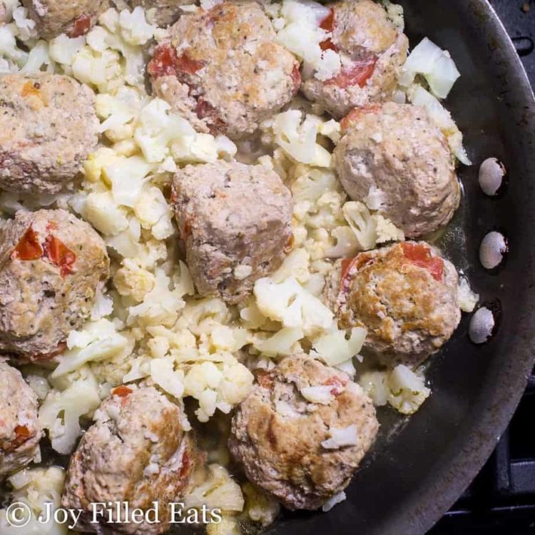 basil & tomato meatballs being cooked in a skillet close up with diced cauliflower