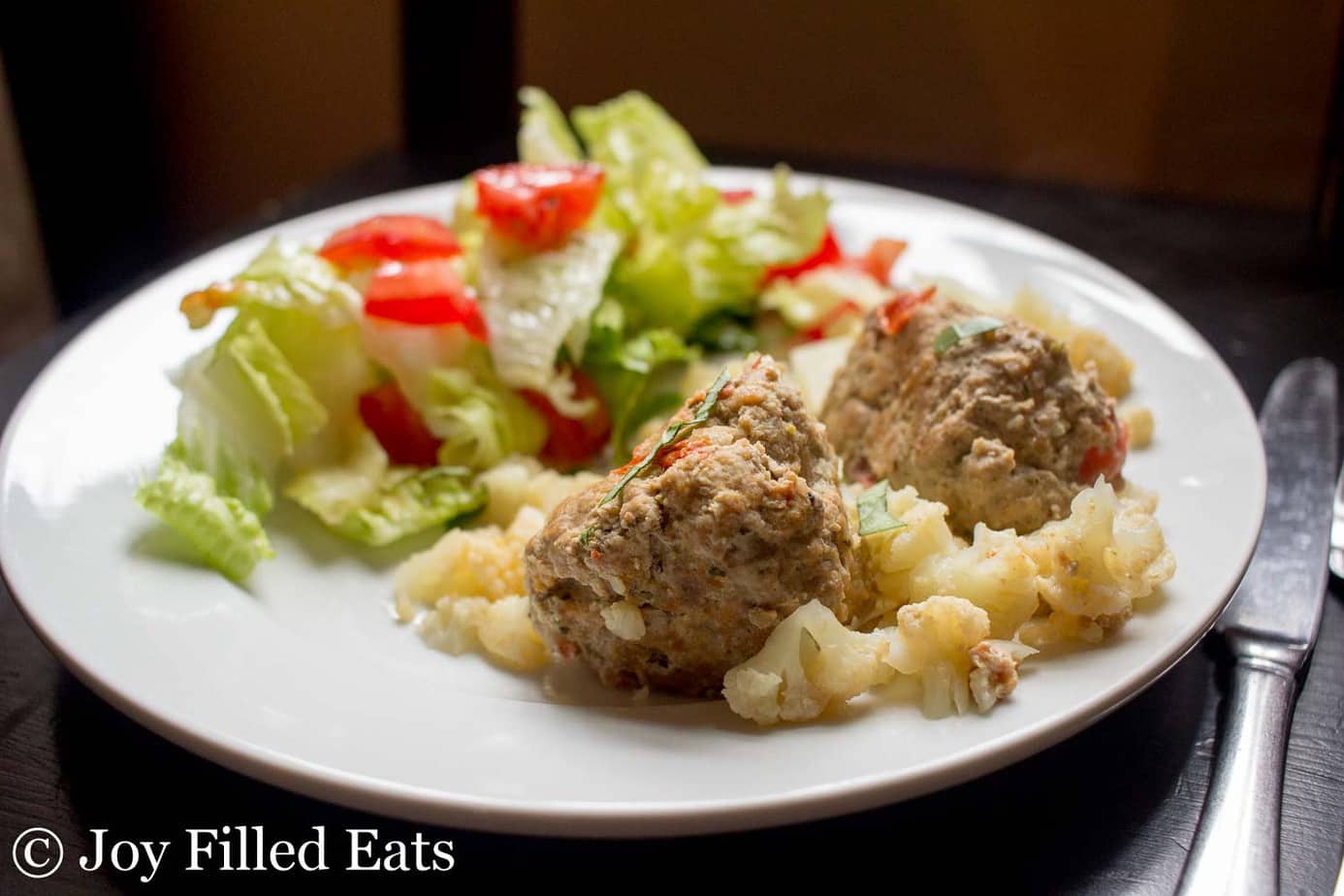 plate with skillet basil & tomato meatballs served over cauliflower with a green salad