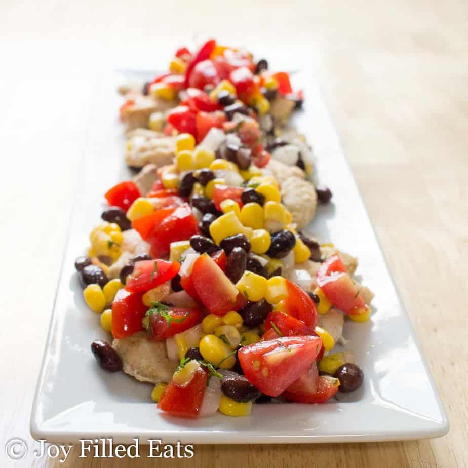 rectangular platter of cumin rubbed chicken topped with black bean and corn salsa