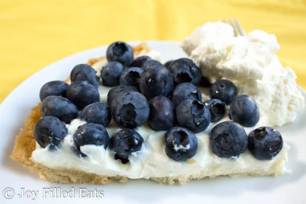 a slice of lemon ricotta pie topped with fresh blueberries and a dollop of whipped cream on a white plate