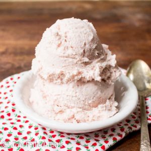 two scoops of ice cream in a white bowl with spoon and strawberry patterned napkin