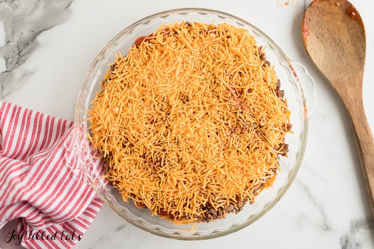 pie plate of taco dip with shredded cheese layer added on tip before baking